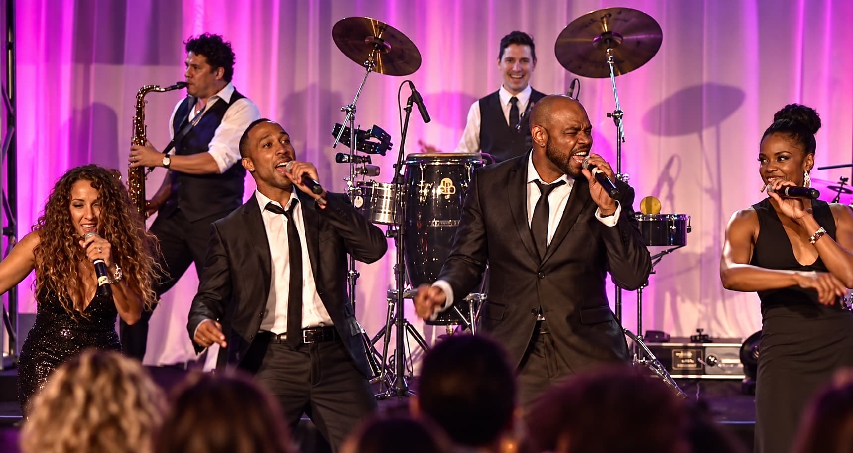 A vocalist in a tuxedo performing against a wall of warm amber stage light